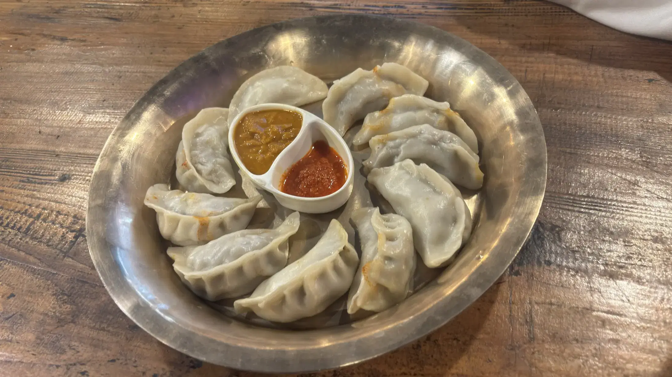 A metal plate of steamed momos served with two dipping sauces