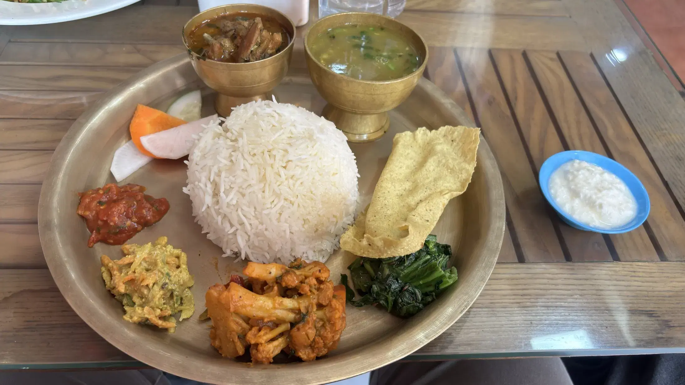 A Nepali dal bhat meal served on a brass plate with rice, lentils, vegetables, pickles, papad, and curd