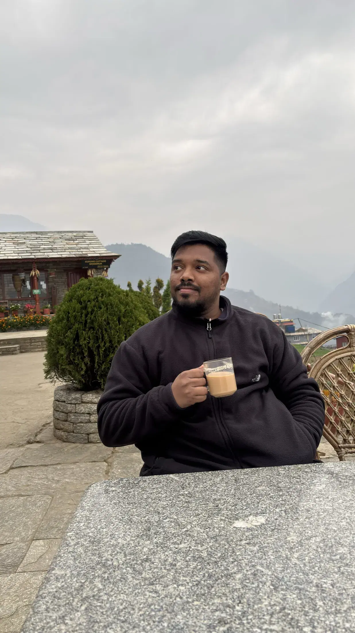 Manish holding a glass of tea in a Ghandruk cottage courtyard
