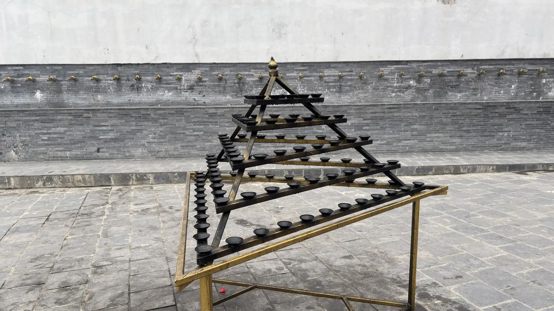 A tiered metal stand holding rows of oil lamps in the temple courtyard