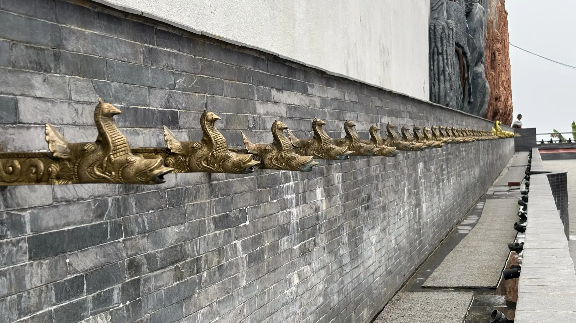 A repeating line of golden bird sculptures mounted along a stone wall at Pumdikot