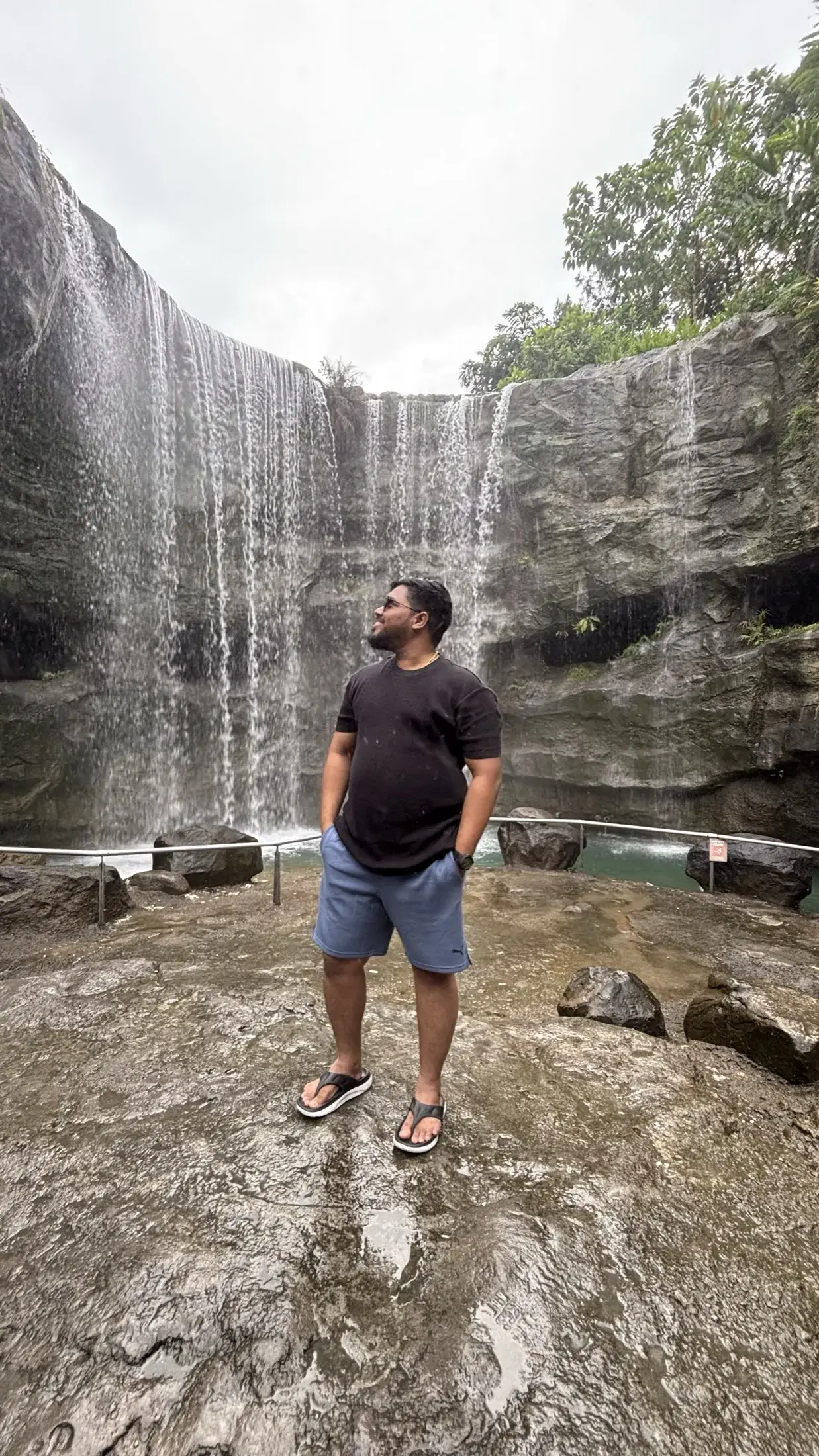 Manish standing in front of a broad waterfall at Singapore Zoo