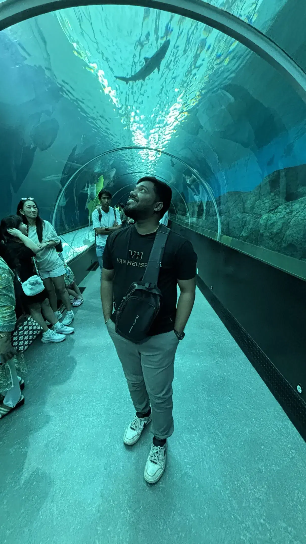 Manish looking up at sharks and fish swimming over an underwater tunnel