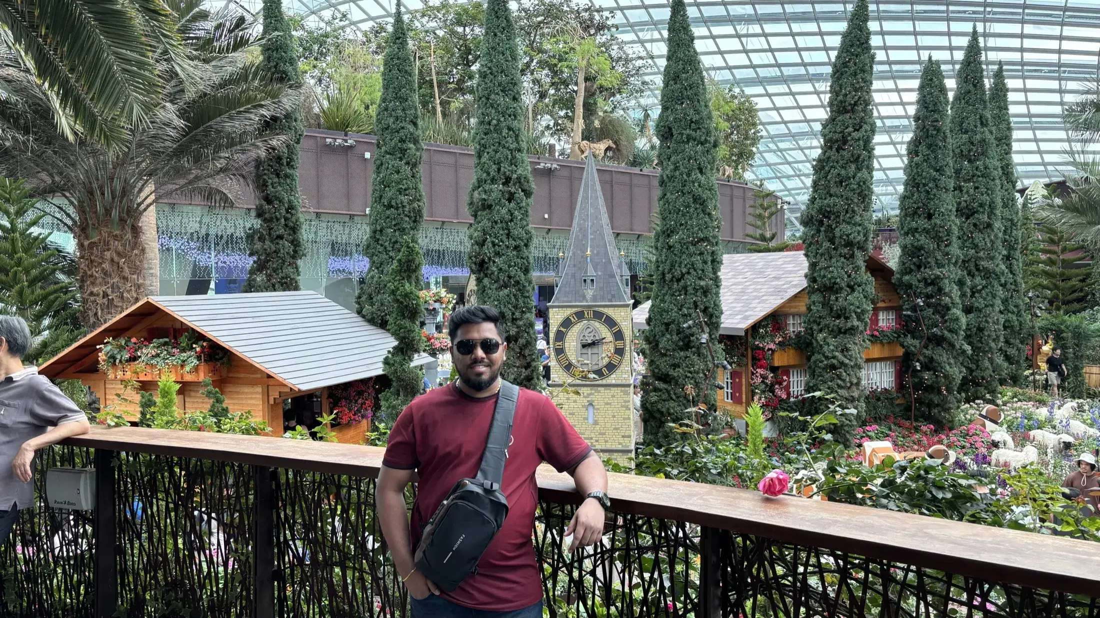 Manish in a conservatory beside a floral display with cottages and a clock tower